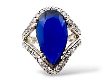 May include: A silver ring featuring a large, teardrop-shaped, deep blue gemstone. The gemstone is surrounded by a halo of smaller, clear stones. The ring has a decorative, openwork design on the band.