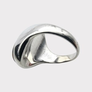 Puede incluir: Un anillo de plata con una parte superior ovalada lisa y redondeada. El anillo est&aacute; hecho de metal pulido y tiene un dise&ntilde;o simple y elegante.