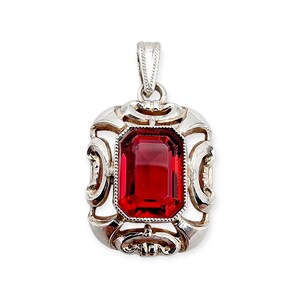 Può includere: Ciondolo in argento con una gemma rossa rettangolare. Il ciondolo presenta un design traforato ornato attorno alla gemma e un'ansa decorativa. La gemma è di un colore rosso intenso e ricco, e il metallo ha una finitura lucida.