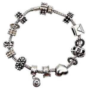 Könnte beinhalten: Ein silbernes Charm-Armband mit verschiedenen dekorativen Anhängern. Zu den Anhängern gehören ein Herz, ein Umschlag und andere geometrische Formen. Das Armband befindet sich auf weißem Hintergrund.