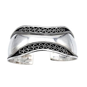 Könnte beinhalten: Ein breites, poliertes Silberarmband. Das Armband hat ein geschwungenes Design mit einem glatten Mittelteil und dekorativen schwarzen Wellenmustern an den oberen und unteren Kanten. Das offene Design ermöglicht ein einfaches Tragen.