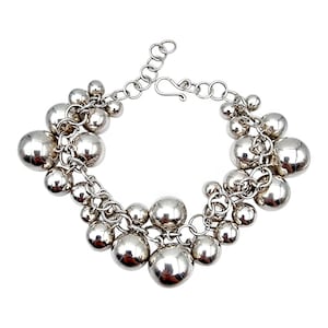 Könnte beinhalten: Ein silbernes Armband mit mehreren runden, glänzenden Kugeln unterschiedlicher Größe. Die Kugeln sind durch eine Kette verbunden, und das Armband hat einen Hakenverschluss. Der Schmuck ist vor einem weißen Hintergrund platziert.