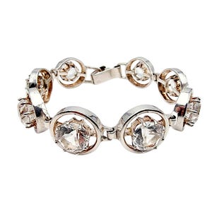 Könnte beinhalten: Silberfarbenes Armband mit klaren, facettierten Edelsteinen, die in kreisförmigen Rahmen gefasst sind. Das Armband hat ein klassisches Design mit einem sicheren Verschluss. Die Edelsteine sind der Blickfang.