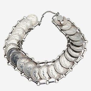 Könnte beinhalten: Ein silbernes Armband aus miteinander verbundenen Münzen. Die Münzen sind alle aus Silber und haben ein erhabenes Profil eines menschlichen Gesichts.