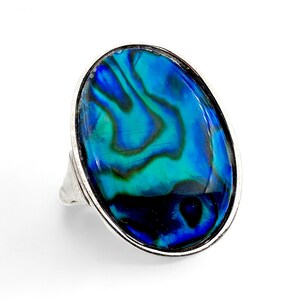 Könnte beinhalten: Ovaler Ring mit einer auffälligen Abalone-Muschel, die wirbelnde Muster in Blau und Grün zeigt. Die Muschel ist in einem silberfarbenen Metallband gefasst. Dieser Ring bietet einen kräftigen Farbtupfer, ideal für jedes Outfit.
