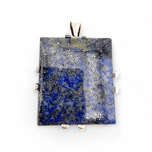 Könnte beinhalten: Rechteckiger Anhänger aus poliertem Lapislazuli mit silbernen Einschlüssen und tiefblauer Farbe. Der Stein ist in einem Silberrahmen mit einer Öse und vier dekorativen Silberakzenten gefasst. Ein Schmuckstück.