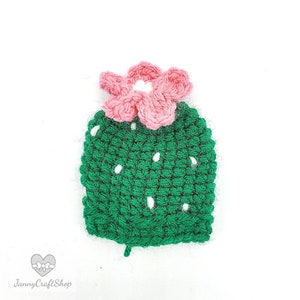 May include: Handmade crochet cactus with a pink flower on top. The cactus is green with white dots, and the flower is a soft pink. The item is likely a decorative piece or an applique for clothing or accessories.