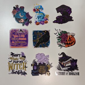 May include: A set of ten Halloween themed stickers featuring various spooky designs. The stickers include a witch's hat, a cauldron, a raven, a pumpkin, and a skull. The stickers are all in a dark color scheme with purple, black, and white accents. The text on the stickers includes "Don't Make Me Flip My Witch Switch", "Creep It Real", "You & Me Scary Movies & Halloween", "Witchey & Bookish", and "Sorta Sweet Sorta Spooky".