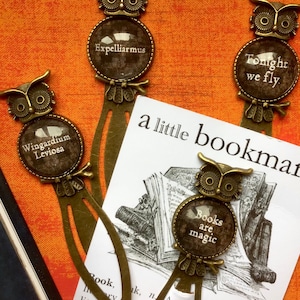 May include: Four owl-shaped bookmarks with bronze metal accents. Each bookmark features a round glass charm with a different Harry Potter-themed quote. The quotes are "Wingardium Leviosa", "Expelliarmus", "Tonight we fly", and "Books are magic".