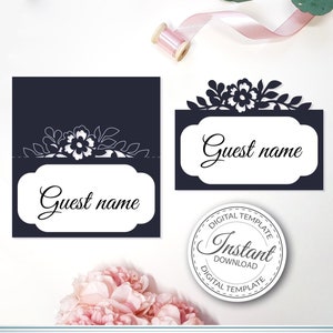 Può includere: Un modello digitale stampabile per un segnaposto da matrimonio. La carta è blu navy con un design floreale bianco e il testo "Nome dell'ospite". Il modello è disponibile per il download immediato.