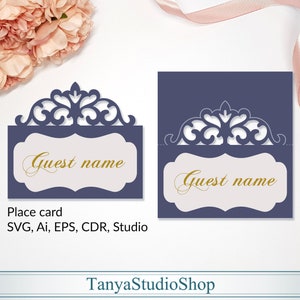 Peut inclure: Une carte de placement bleue avec un design décoratif, orné et découpé. La carte a un fond blanc avec le texte "Guest name" en lettres dorées. Le texte "Place card" et "SVG, Ai, EPS, CDR, Studio" est également inclus. La carte est conçue par TanyaStudioShop.