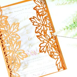 Puede incluir: Una invitaci&oacute;n de boda cortada con l&aacute;ser con un tema oto&ntilde;al. La invitaci&oacute;n es naranja con fondo blanco y presenta un dise&ntilde;o de hojas alrededor de los bordes. El texto de la invitaci&oacute;n dice "Rachel & Carl".