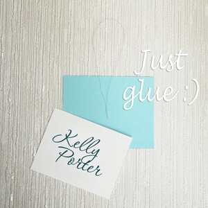 May include: A white card with the text "Kelly Porter" written in teal cursive. A light blue card with the text "Just glue :)" written in white cursive is on top of the white card.