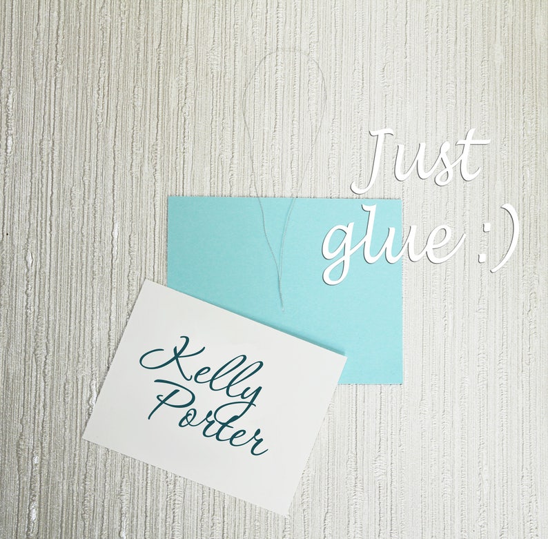 May include: A white card with the text "Kelly Porter" written in teal cursive. A light blue card with the text "Just glue :)" written in white cursive is on top of the white card.