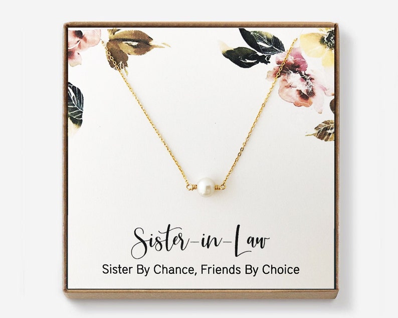 Puede incluir: Un collar de oro con un solo colgante de perla en una caja de regalo. La caja tiene un dise&ntilde;o floral y el texto "Sister-in-Law Sister By Chance, Friends By Choice".
