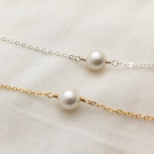 May include: Two delicate necklaces with single pearl pendants. One necklace has a silver chain and the other has a gold chain.