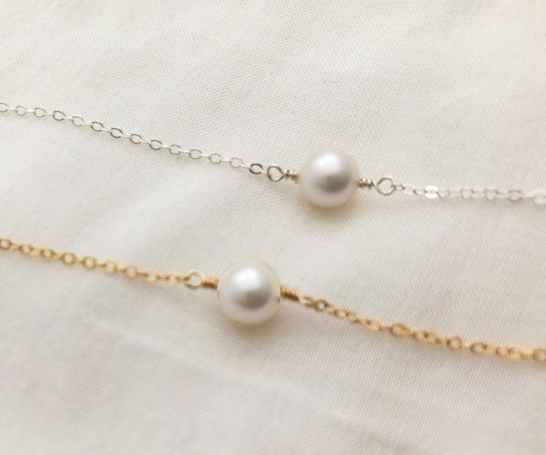 May include: Two delicate necklaces with single pearl pendants. One necklace has a silver chain and the other has a gold chain.