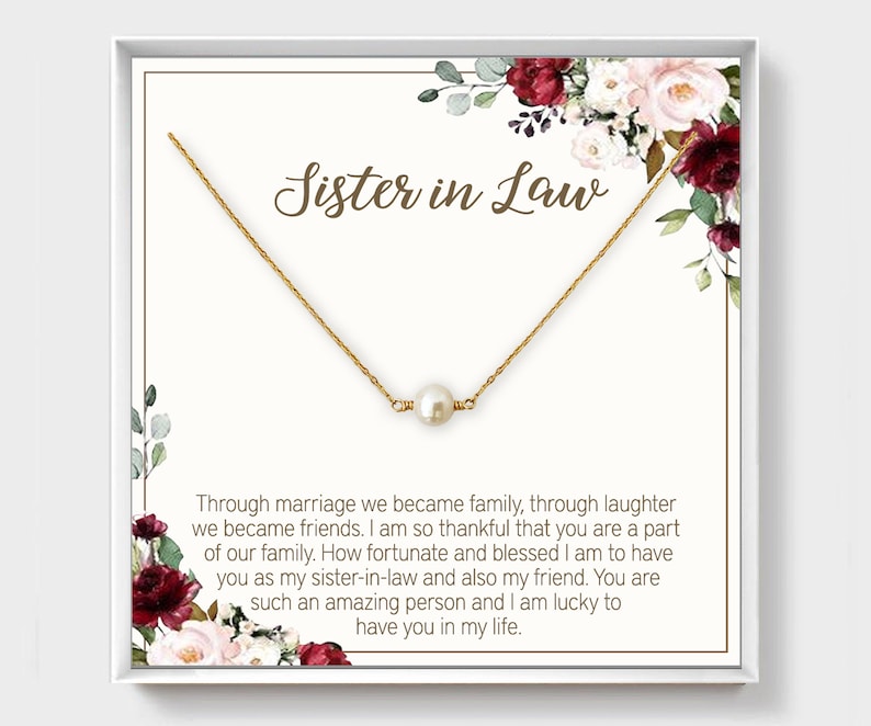 May include: A white card with a gold necklace and a single pearl pendant. The card has a floral design and the text "Sister in Law" in brown lettering. The text on the card reads: "Through marriage we became family, through laughter we became friends. I am so thankful that you are a part of our family. How fortunate and blessed I am to have you as my sister-in-law and also my friend. You are such an amazing person and I am lucky to have you in my life."
