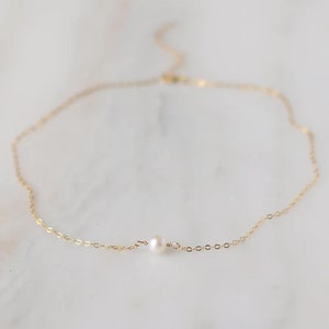 Puede incluir: Un delicado collar de cadena de oro con un peque&ntilde;o colgante de perla.
