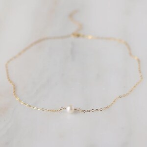 May include: A delicate gold chain necklace with a single small pearl pendant.