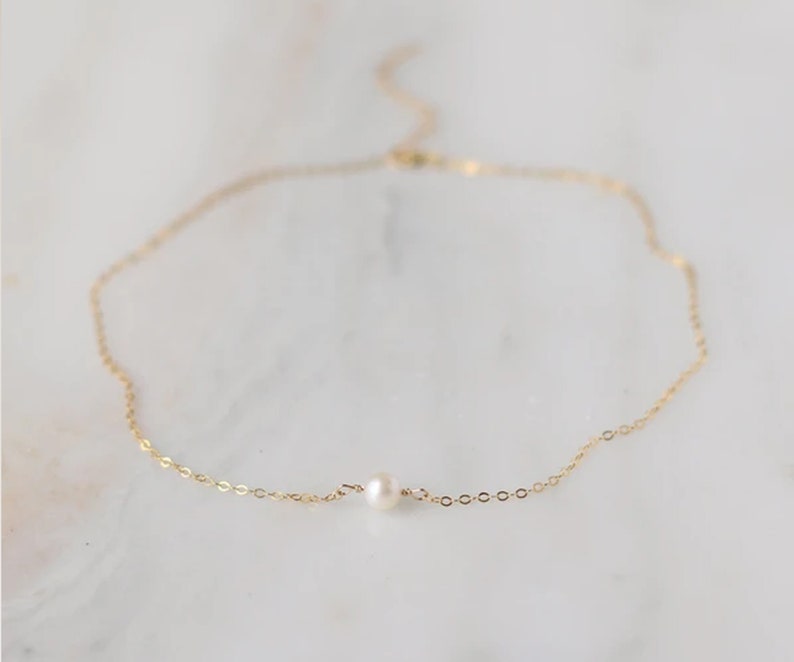 May include: A delicate gold chain necklace with a single small pearl pendant.
