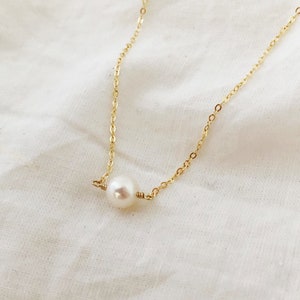 May include: A delicate gold chain necklace with a single white pearl pendant.