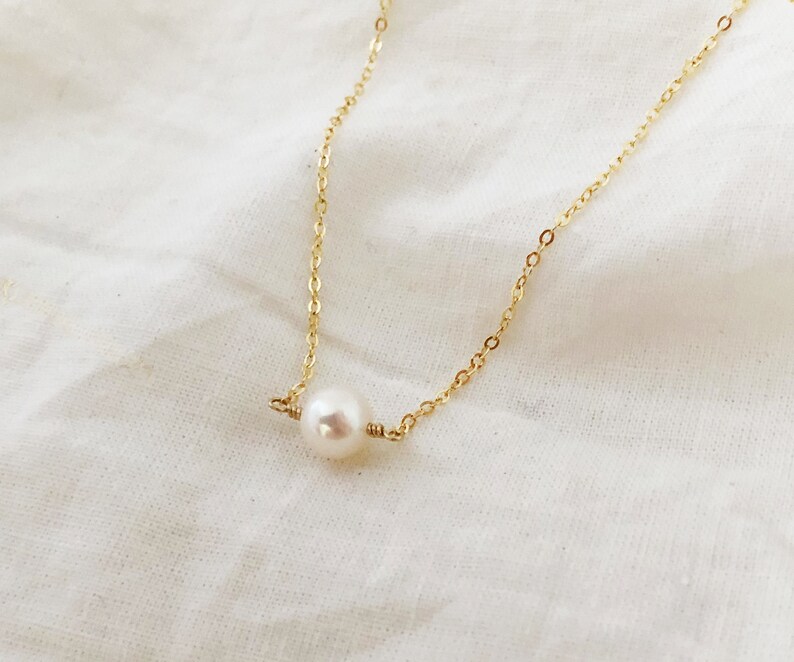 May include: A delicate gold chain necklace with a single white pearl pendant.