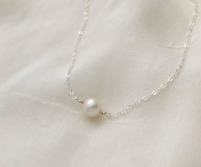 Puede incluir: Un delicado collar de cadena de plata con un solo colgante de perla blanca.