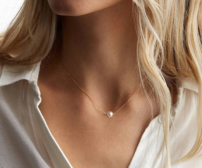 May include: A delicate gold chain necklace with a single white pearl pendant.