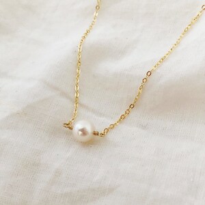 Puede incluir: Un delicado collar de cadena dorada con un solo colgante de perla blanca.