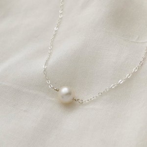 May include: A delicate silver chain necklace with a single white pearl pendant.