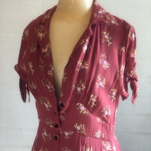 Peut inclure: Une longue robe &agrave; fleurs rouge &agrave; imprim&eacute; floral avec un devant boutonn&eacute; et des manches courtes. La robe a un corsage ajust&eacute; et une jupe ample.