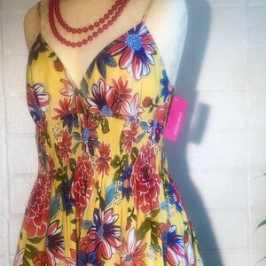 Peut inclure: Robe d'été jaune à motifs floraux rouges, bleus et blancs. La robe a un corsage ajusté et une jupe évasée. Un collier de perles rouges est drapé sur l'encolure. L'étiquette indique "xhilaration".