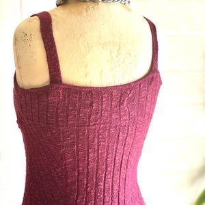 May include: A burgundy ribbed knit vest top with wide straps is displayed on a mannequin. A silver chain necklace is around the mannequin's neck. The vest top has a textured, vertical ribbed pattern.