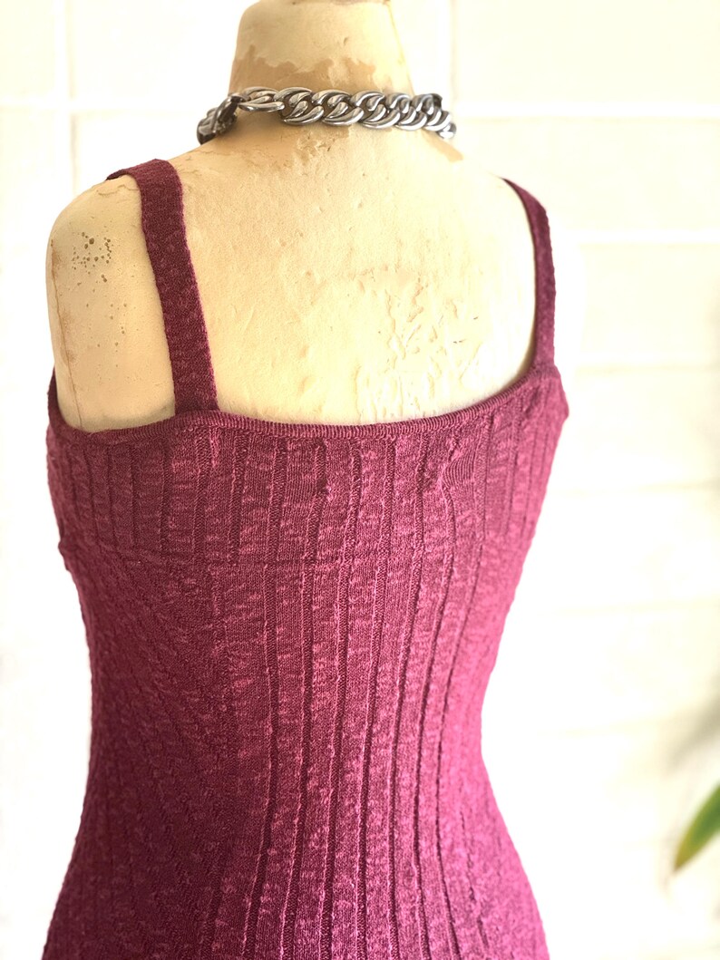 May include: A burgundy ribbed knit vest top with wide straps is displayed on a mannequin. A silver chain necklace is around the mannequin's neck. The vest top has a textured, vertical ribbed pattern.