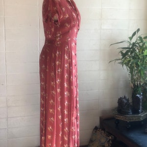 Peut inclure: Une longue robe de couleur rouille &agrave; imprim&eacute; floral. La robe a un devant boutonn&eacute;, un col en V et des manches courtes. La robe est sur un mannequin.