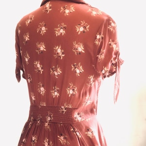 Peut inclure: Une robe midi de couleur rouille &agrave; imprim&eacute; floral et taille cintr&eacute;e. La robe a des manches courtes avec un d&eacute;tail de n&oelig;ud &agrave; la manchette.