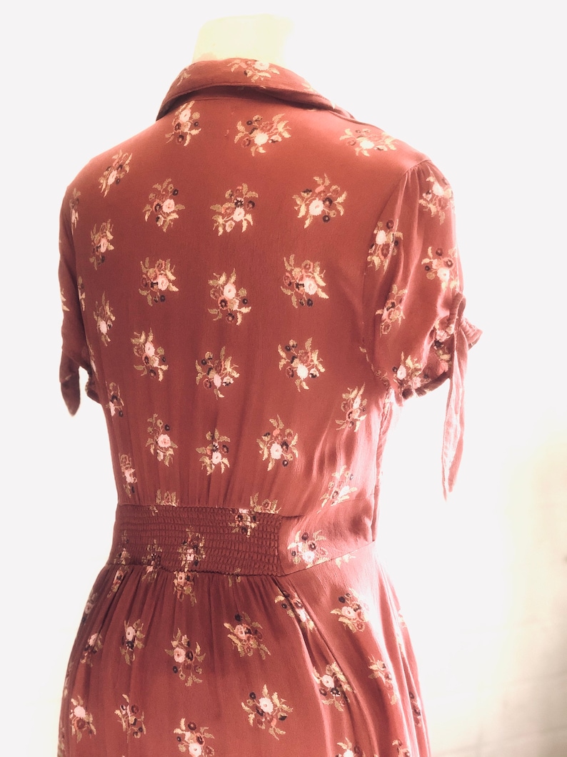 Peut inclure: Une robe midi de couleur rouille &agrave; imprim&eacute; floral et taille cintr&eacute;e. La robe a des manches courtes avec un d&eacute;tail de n&oelig;ud &agrave; la manchette.