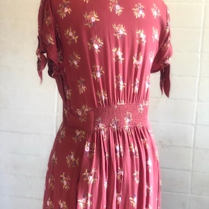 Peut inclure: Une robe midi de couleur rouille &agrave; imprim&eacute; floral. La robe a un col, des manches courtes et un corsage ajust&eacute;. La jupe est fronc&eacute;e &agrave; la taille et coule jusqu'&agrave; l'ourlet.