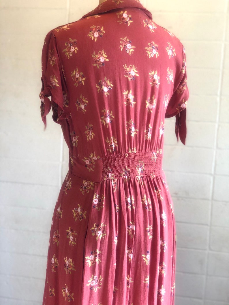 Peut inclure: Une robe midi de couleur rouille &agrave; imprim&eacute; floral. La robe a un col, des manches courtes et un corsage ajust&eacute;. La jupe est fronc&eacute;e &agrave; la taille et coule jusqu'&agrave; l'ourlet.