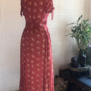 Peut inclure: Une longue robe maxi de couleur rouille &agrave; imprim&eacute; floral et manches courtes. La robe a un devant boutonn&eacute; et une ceinture &agrave; la taille.