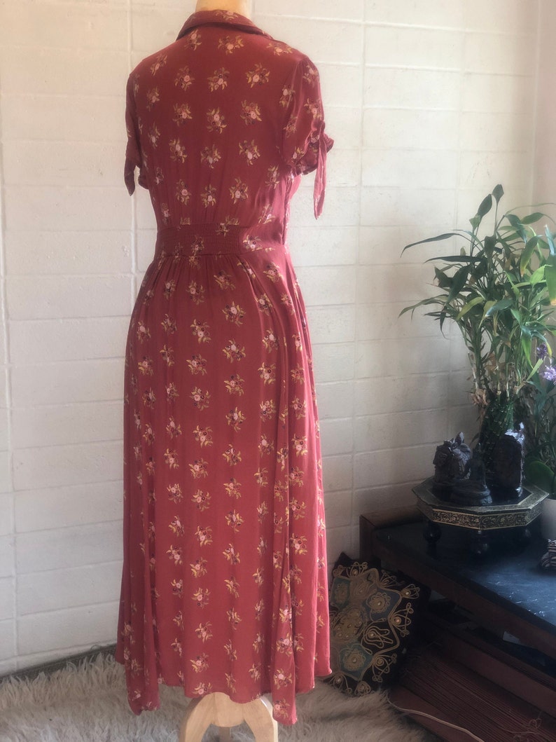 Peut inclure: Une longue robe maxi de couleur rouille &agrave; imprim&eacute; floral et manches courtes. La robe a un devant boutonn&eacute; et une ceinture &agrave; la taille.