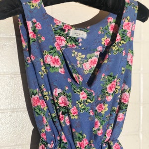 Può includere: Abito blu senza maniche con un motivo floreale di rose rosa e foglie verdi. L'abito ha uno scollo a V, una chiusura con bottoni e una vita arricciata. L'etichetta recita "initial J".