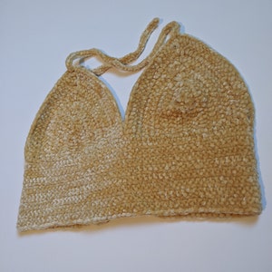 May include: A beige crocheted halter top with a v-neckline. The top is made of a soft, fuzzy yarn.