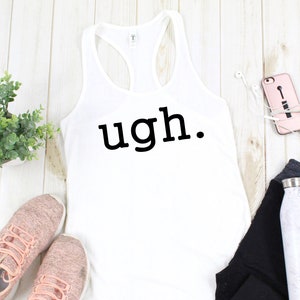 May include: White racerback tank top with the word "ugh." in black. The tank top is next to pink sneakers, black leggings, a water bottle, a phone in a pink case, and a small green plant.
