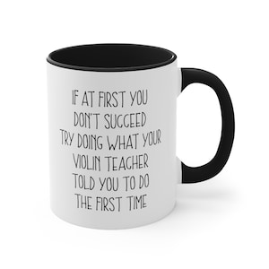 May include: White coffee mug with a black rim and handle. The mug has black text that reads "If at first you don't succeed try doing what your violin teacher told you to do the first time."
