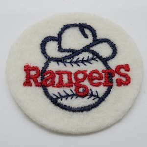 May include: A circular white felt patch featuring an embroidered design of a navy blue cowboy hat resting on top of a baseball. The word Rangers is stitched across the center of the baseball in bold red thread with navy blue stitching details.