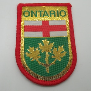 May include: A rectangular embroidered patch with a red border featuring the word ONTARIO in green letters at the top. The design includes a white section with a red cross above a green section containing three gold maple leaves on a single branch.