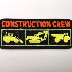 May include: A rectangular black embroidered patch featuring the orange text CONSTRUCTION CREW at the top. Below the text, three separate green-outlined boxes contain yellow embroidered illustrations of a tractor, an excavator, and a dump truck.