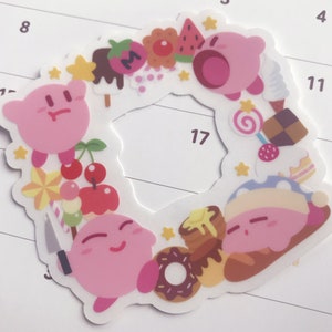 May include: A pink and white sticker featuring a circle of pink cartoon characters with various food and dessert items surrounding them. The characters are wearing different outfits and expressions. The sticker is on a white calendar with numbers.